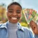 Young african american woman smiling happy holding south africa rand banknotes at the city.